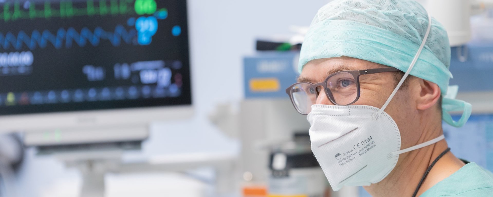 Anästhesist mit Schutzmaske beobachtet die Vitalwerte eines Patienten auf dem Monitor