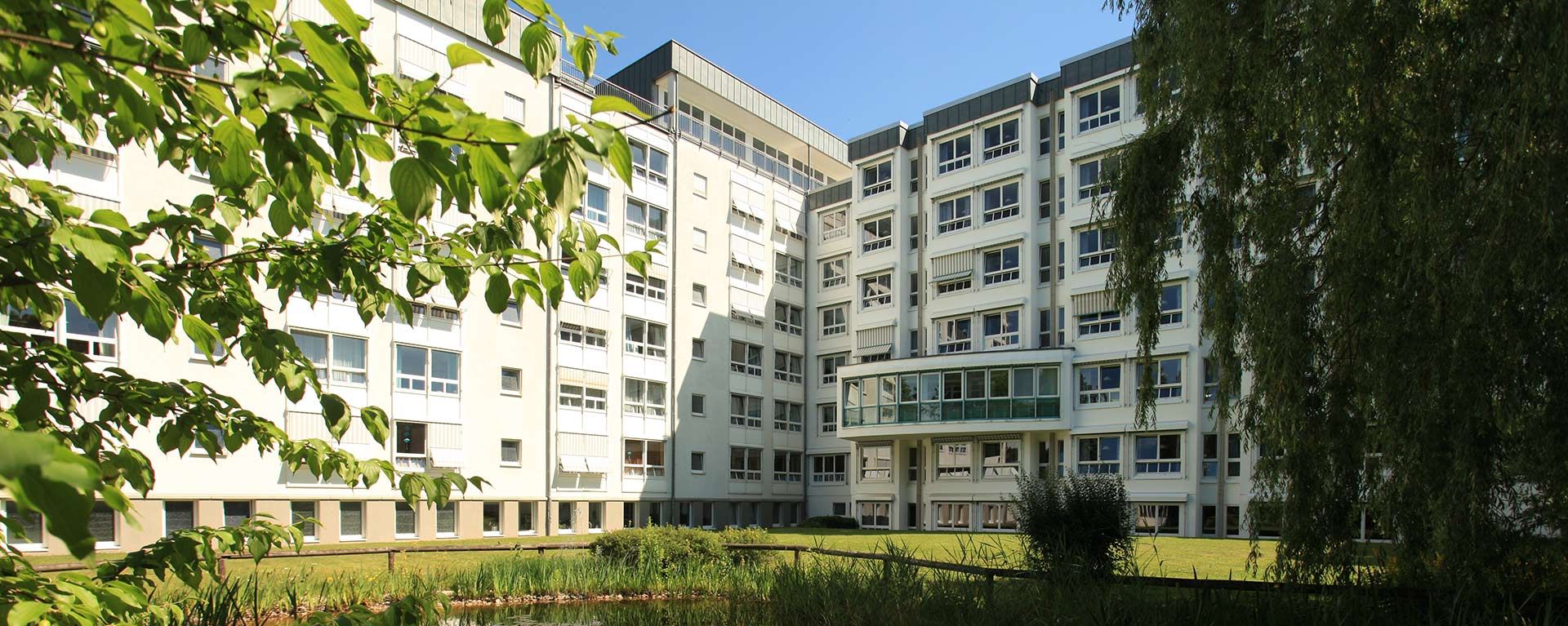 Aussenansicht der Klinik Mindelheim mit Teich und Bäumen der Parkanlage im Vordergrund