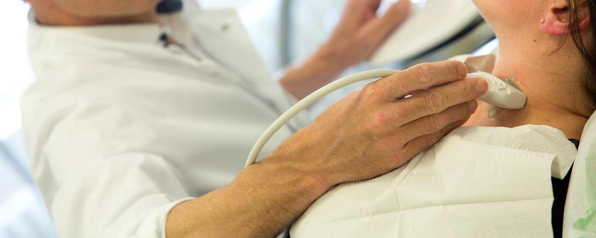 Ein Arzt der Allgmeneinchirurgie untersucht den Hals einer Patientin mit dem Ultraschallgerät