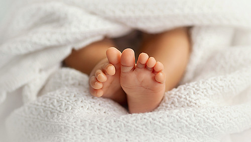 Adorable baby feet covered in a white blanket, maternity and bab