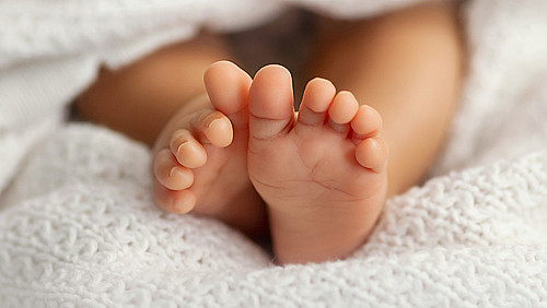 Adorable baby feet covered in a white blanket, maternity and bab