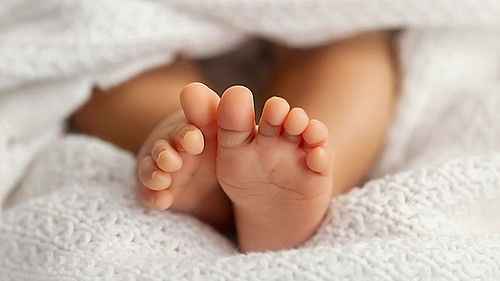 Adorable baby feet covered in a white blanket, maternity and bab