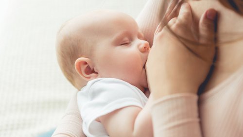 cropped view of mother breastfeeding her child in apartment