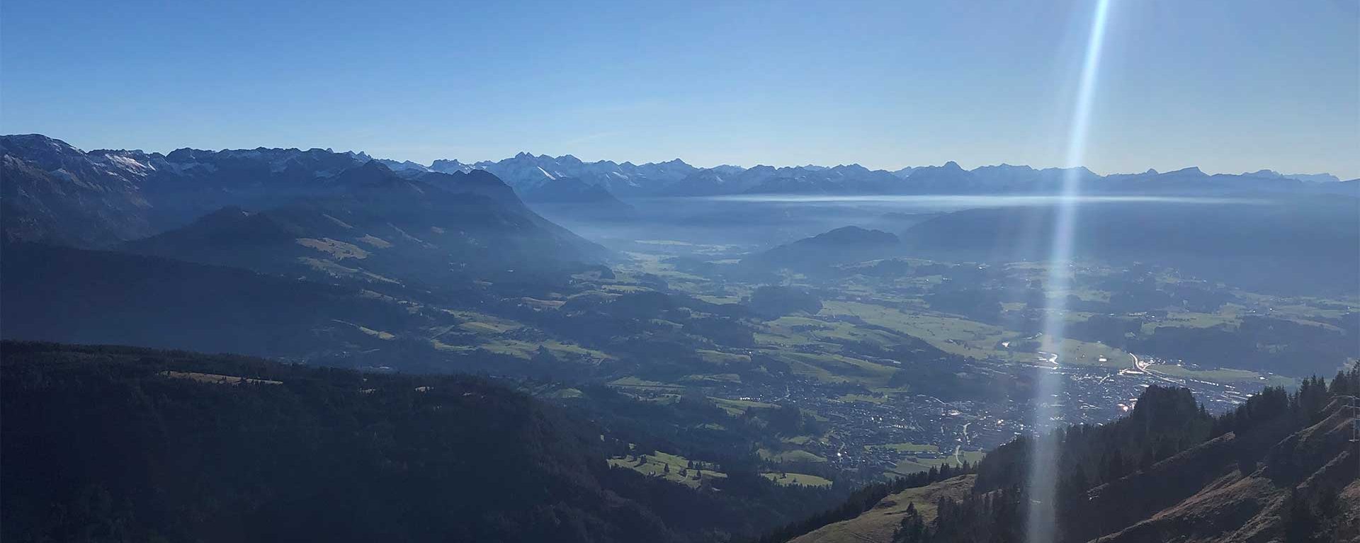 Panoramablick über das Allgäu mit Bergen, Tälern und der Sonne am klaren Himmel – landschaftliches Motiv für den Klinikverbund Allgäu.