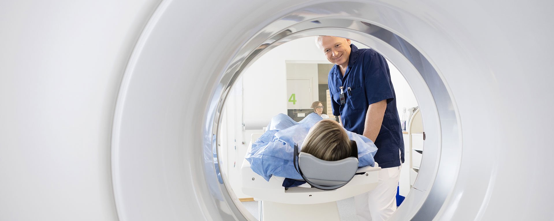 Radiologie und Röntgendiagnostik in Mindelheim Männlicher Arzt des Klinikverbunds Allgäu betrachtet eine Patientin, die einen CT-Scan durchläuft.