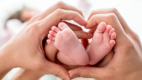 newborn baby feet on mom and dad hands, shape like a lovely heart. happy family concept