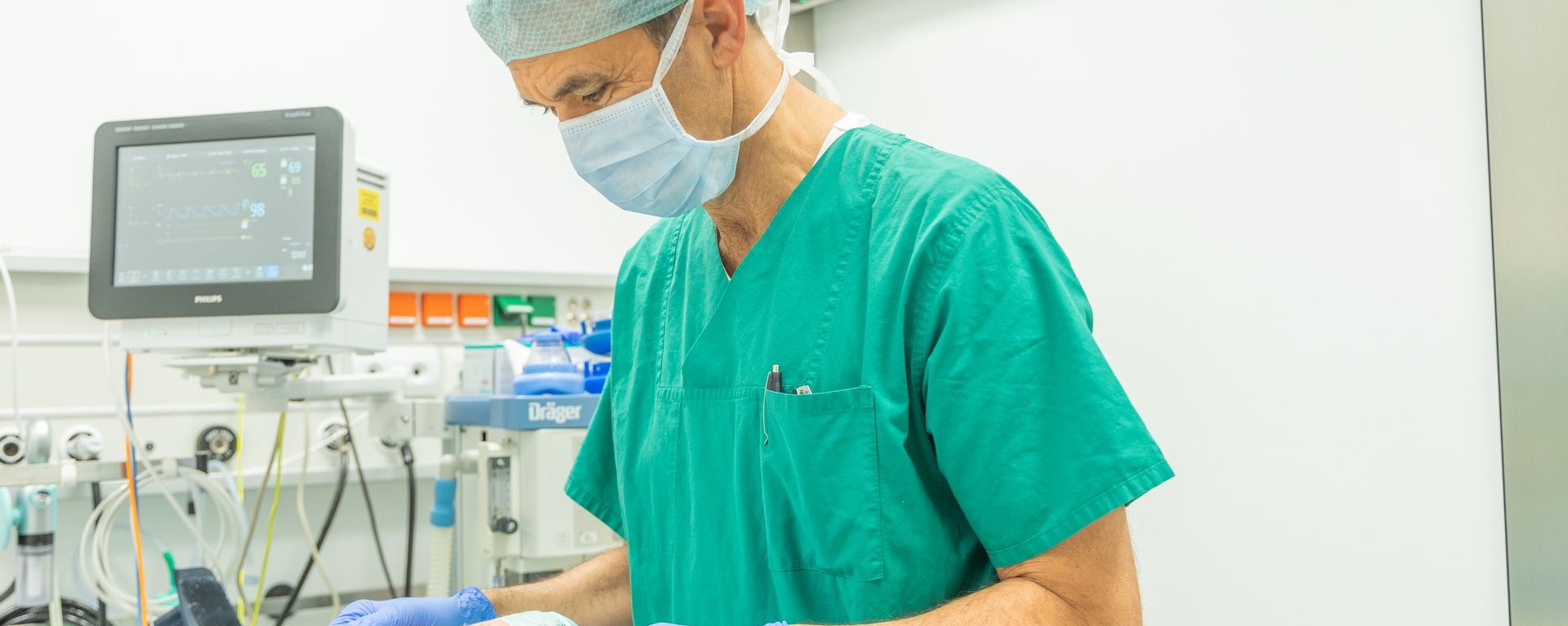 Anästhesist in grüner OP-Kleidung überprüft bei einem Patienten die Beatmung im Operationssaal.