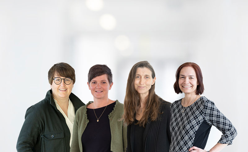 Gruppenfoto von vier Personen aus dem Ethikkomitee, die lächelnd in die Kamera blicken. Alle tragen Alltagskleidung und stehen vor einem hellen, unscharfen Hintergrund.