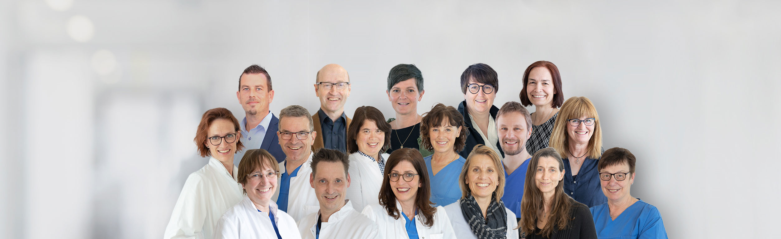 Gruppenfoto des interdisziplinären Ethikkomitees: Mehrere Frauen und Männer aus Medizin, Pflege, Psychologie und Verwaltung stehen in zwei Reihen vor einem hellen, unscharfen Klinik-Hintergrund und lächeln in die Kamera.